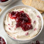 Cranberry cream cheese dip in a white bowl, topped with cranberry sauce and served with crackers.