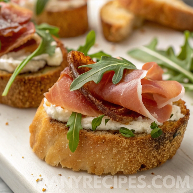 boursin-prosciutto-arugula-crostini (1) Toasted crostini topped with Boursin cheese, prosciutto, and fresh arugula leaves.