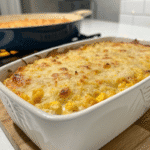 Golden-brown sweet corn casserole topped with melted cheese in a white ceramic baking dish.