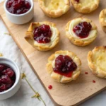 Baked Brie Bites with Cranberry 12 Close-up of baked brie bites with cranberry on a wooden board with extra cranberry sauce on the side.
