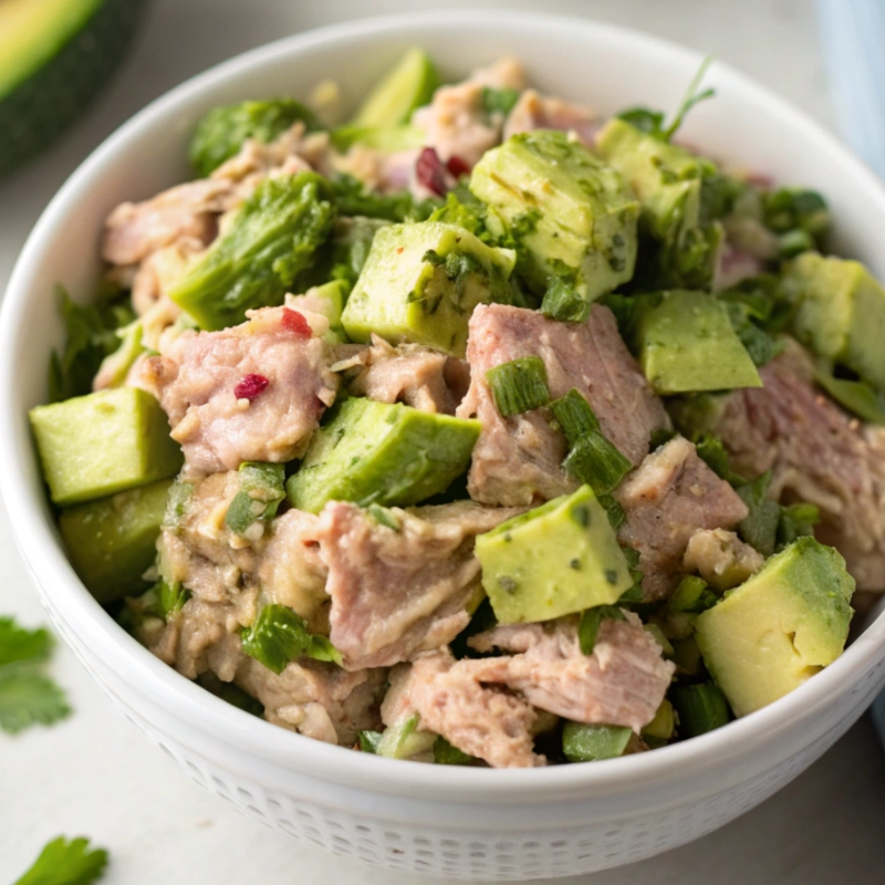 Bowl of avocado tuna salad with diced avocado, tuna, fresh herbs, and chopped vegetables.