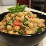 Couscous salad with chickpeas, spinach, cherry tomatoes, and fresh herbs in a black bowl.