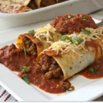 Two beef enchiladas topped with shredded cheese and red enchilada sauce on a white plate.