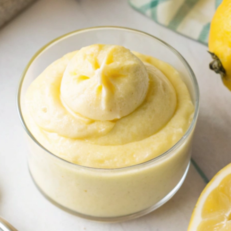 Thick and creamy lemon mousse piped into a clear dessert cup, surrounded by fresh lemons.