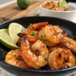 Grilled shrimp glazed with honey lime sauce, served in a black bowl with lime wedges.
