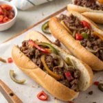 Ground beef cheesesteak sandwiches topped with red and green bell peppers on parchment paper.