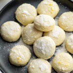 Overhead view of powdered sugar-coated Meyer lemon meltaway cookies on a black plate.