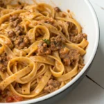 Fettuccine pasta with creamy meat sauce in a white bowl.