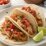 Soft flour tortillas filled with shredded slow-cooked chicken, topped with diced tomatoes, onions, and fresh cilantro, served with lime wedges.