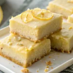 Stack of lemon truffle blondies drizzled with lemon glaze on a ceramic plate.