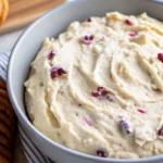Close-up of creamy sweet heat appetizer dip with cranberries swirled in a light blue bowl.