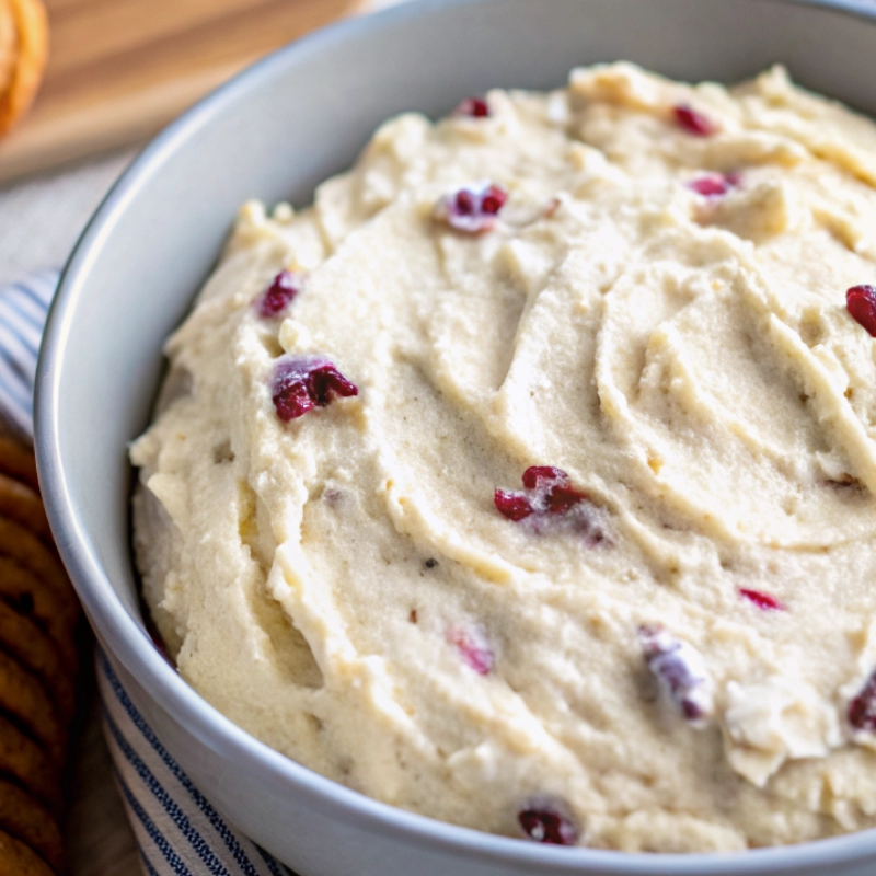 Close-up of creamy sweet heat appetizer dip with cranberries swirled in a light blue bowl.